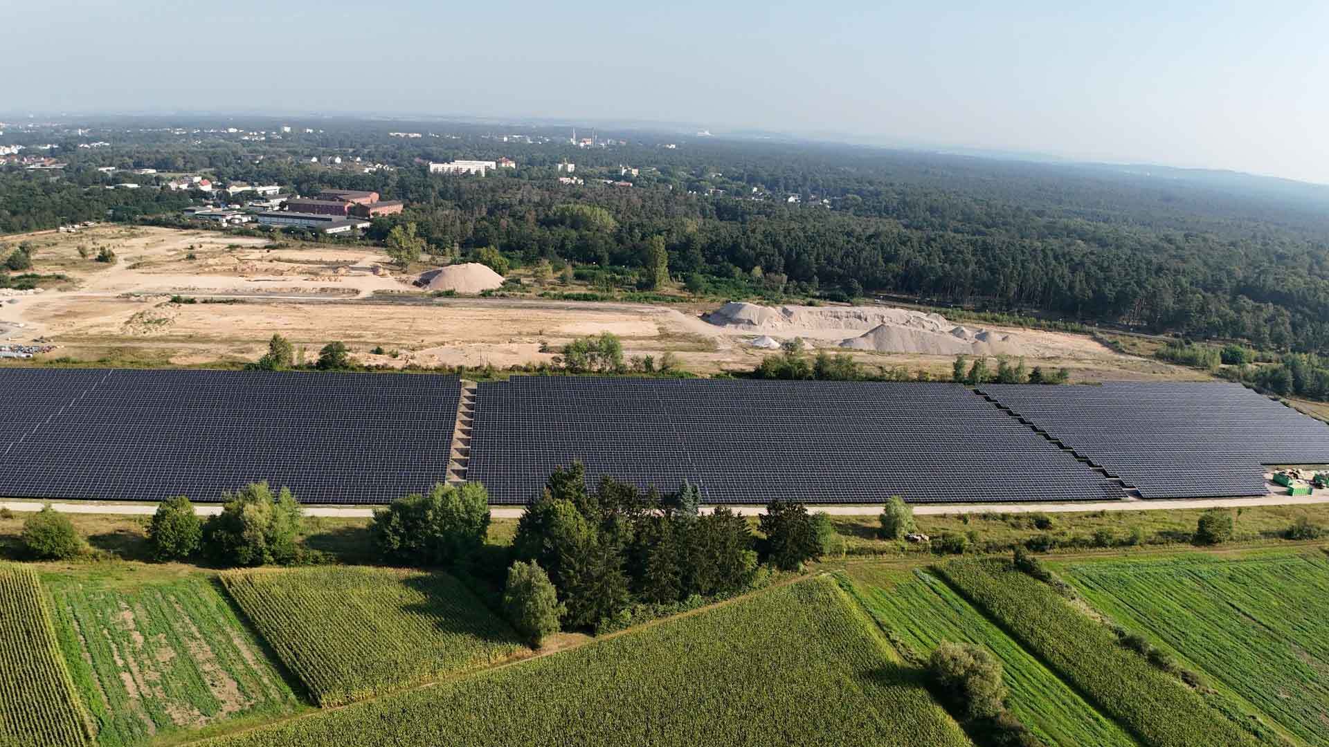 Luftaufnahme eines großen Solarfelds am Waldrand mit angrenzenden Feldern.